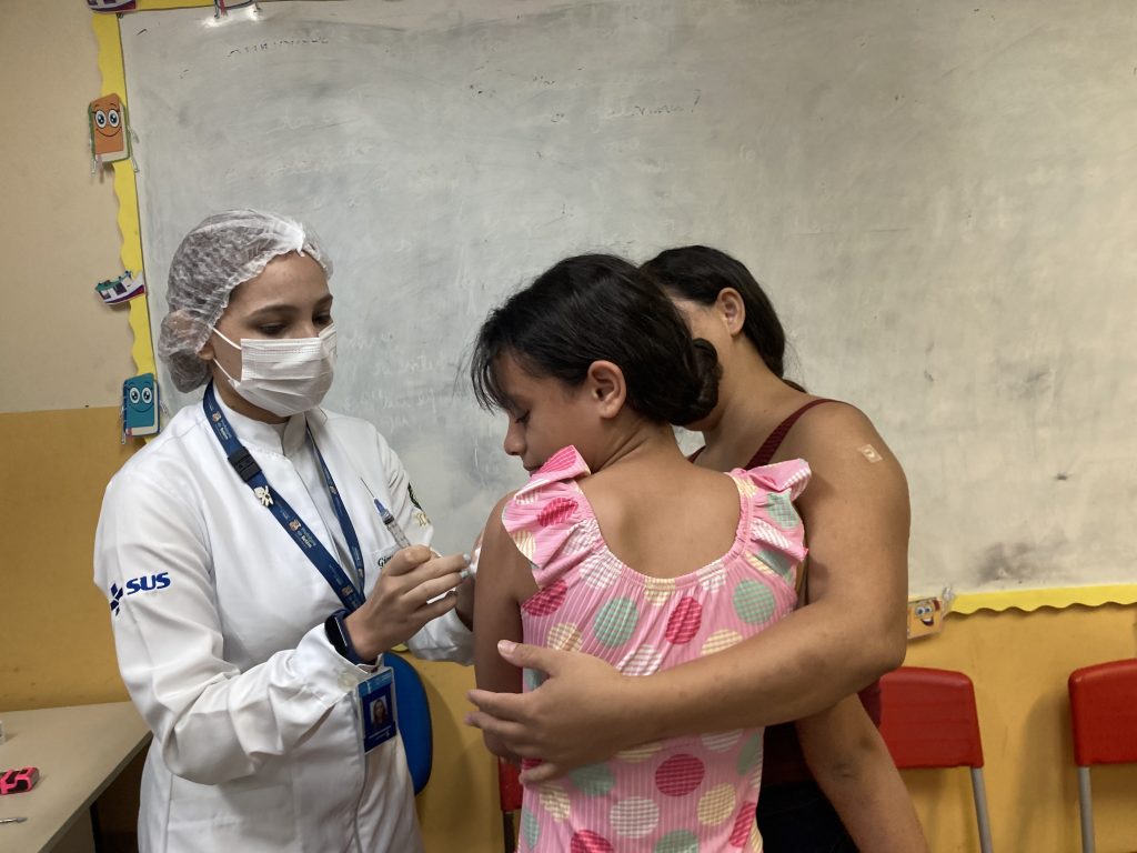 dona de casa Ângela dos Santos consola a filha Vitória durante a aplicação da vacina contra a Covid